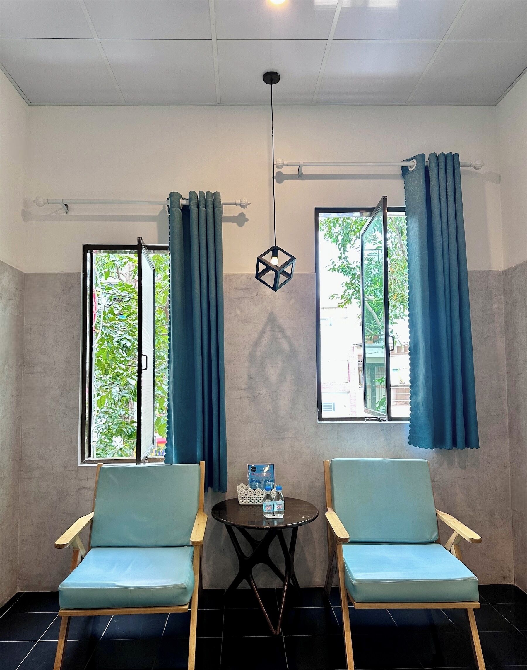 Una habitación con dos sillas azul claro, una pequeña mesa con botellas de agua y una lámpara colgante.