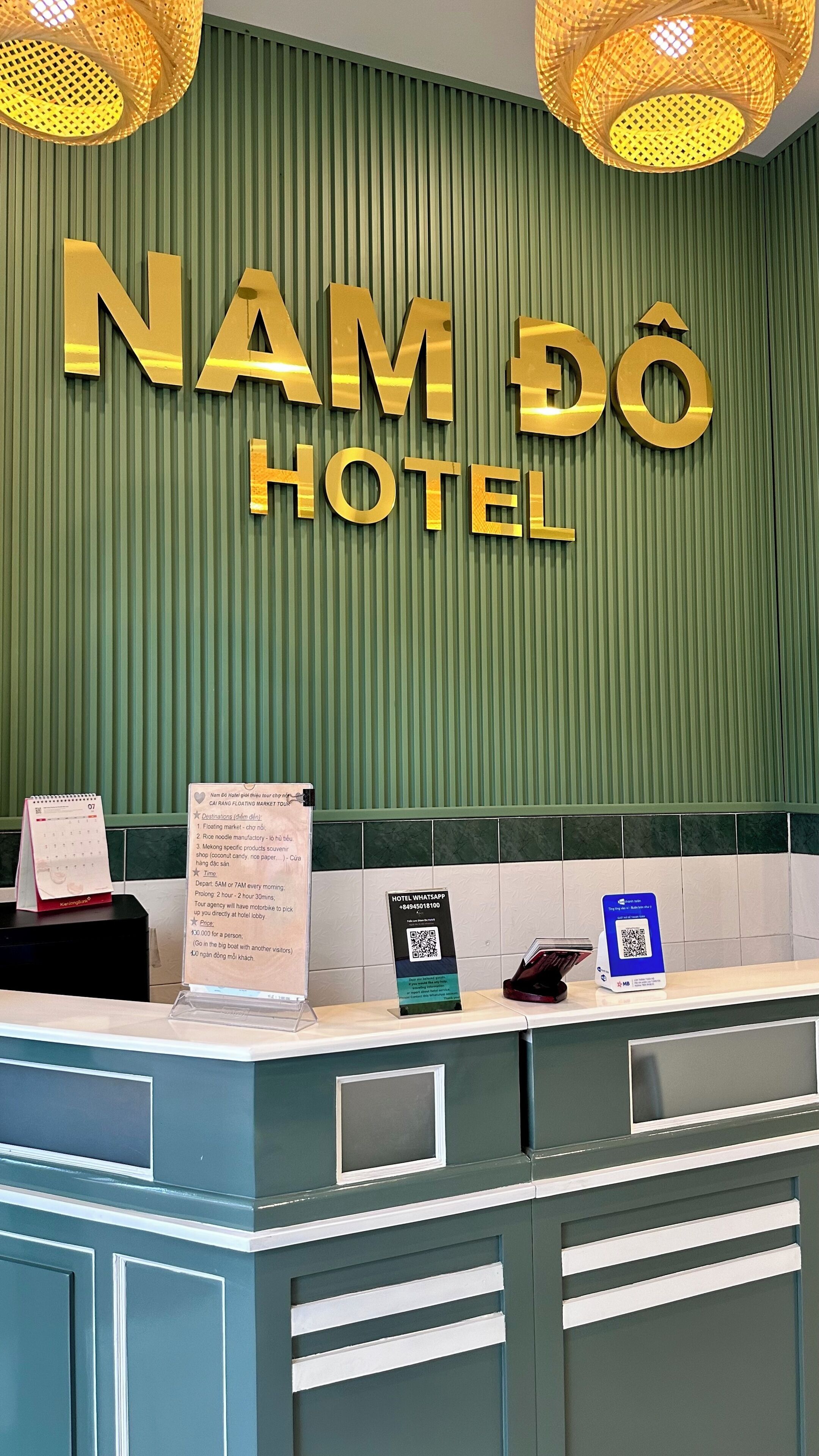 A hotel reception desk with a green wall and a sign that reads 'NAM DÔ HOTEL'.