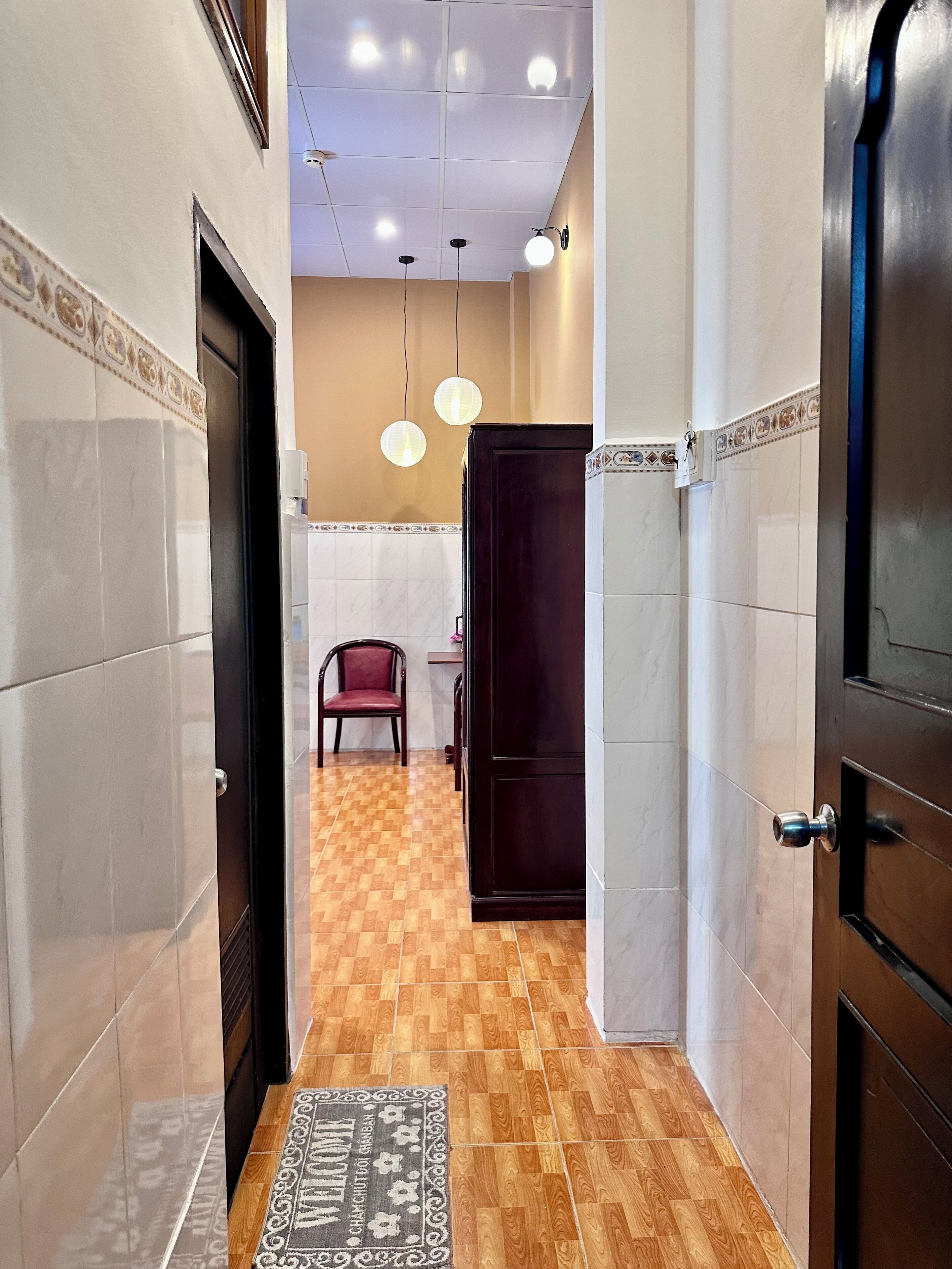 A hallway with a wooden floor, a red chair, a dark wooden door, and a tiled wall with a decorative border.