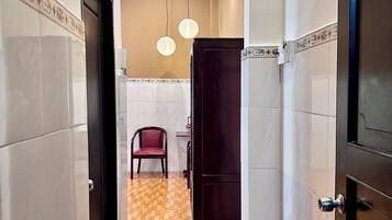 A hallway with a wooden floor, a red chair, a dark wooden door, and a tiled wall with a decorative border.