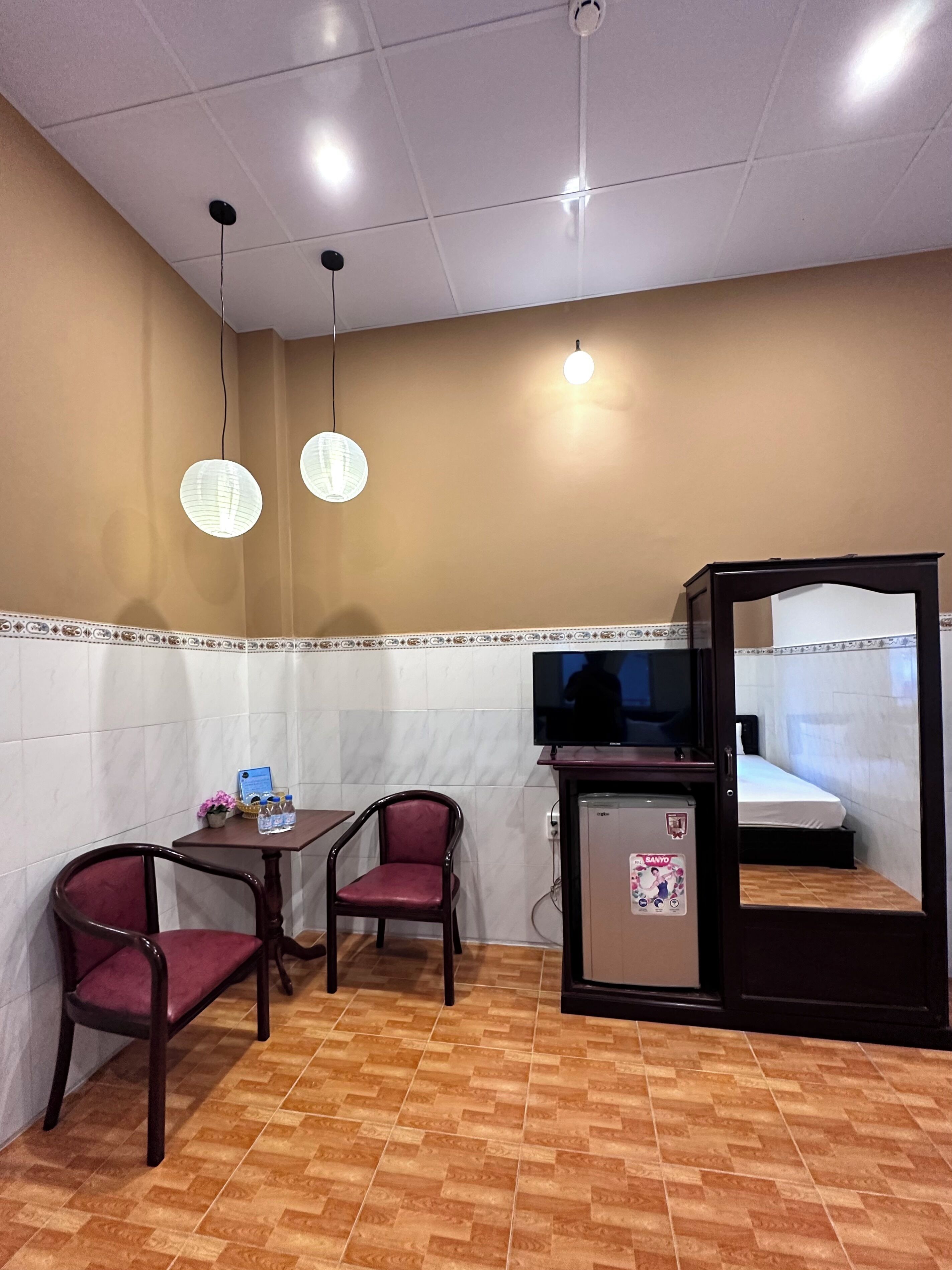 Una habitación compacta con cama, televisor, refrigerador pequeño y dos sillas.