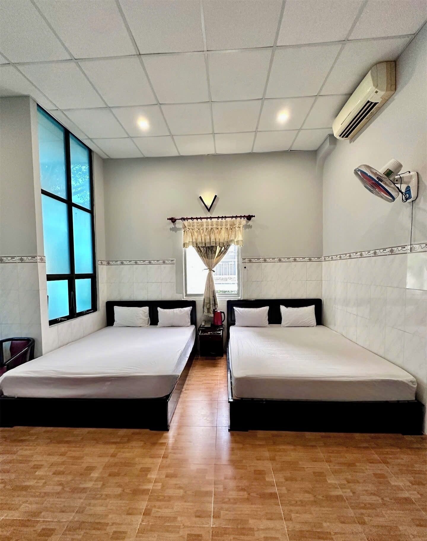 A hotel room with two single beds, a large window, a chandelier, and an air conditioning unit.