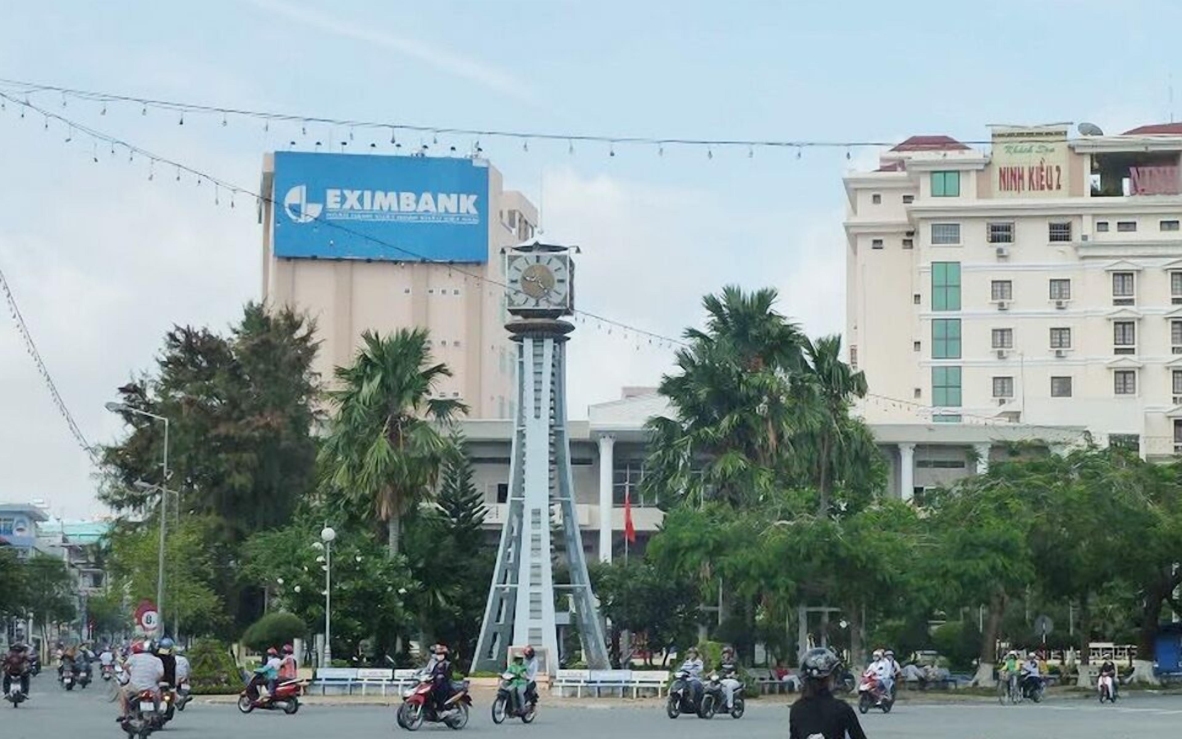 A clock tower with a blue sign for Eximbank in the background.