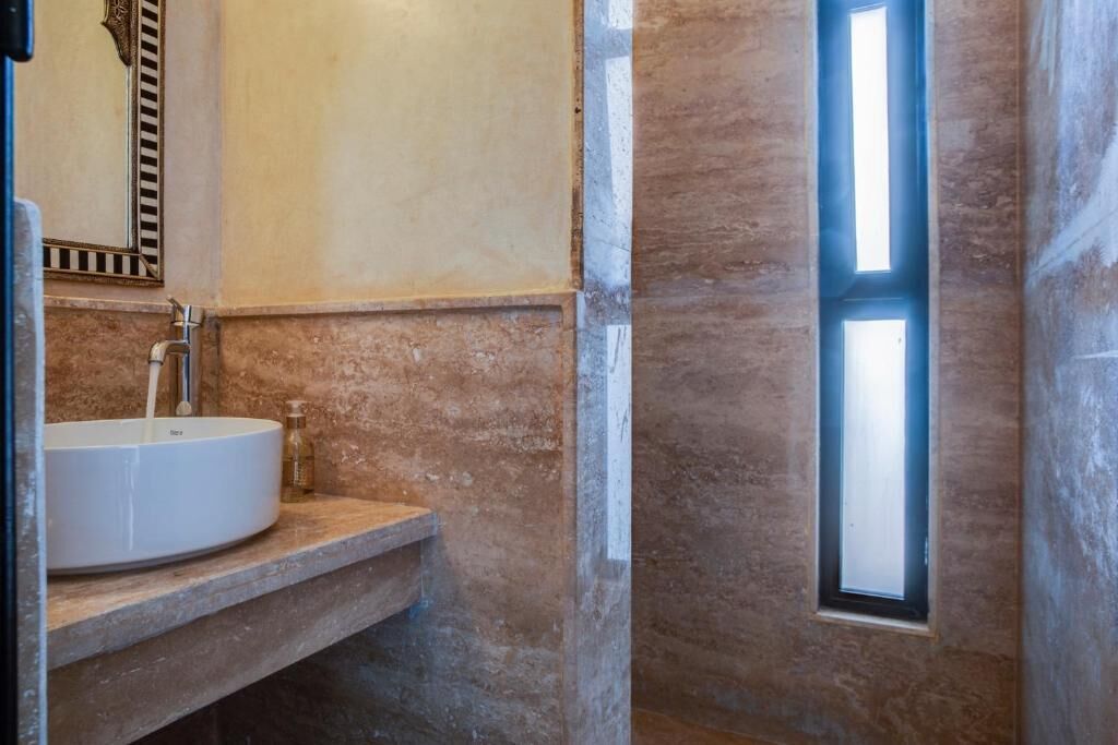 A bathroom with a white sink, a mirror, and a window.