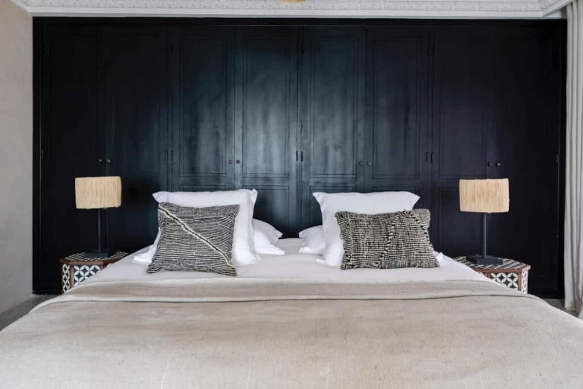 A double bed with a beige blanket, two bedside tables with patterned lamps, and a dark wooden headboard.