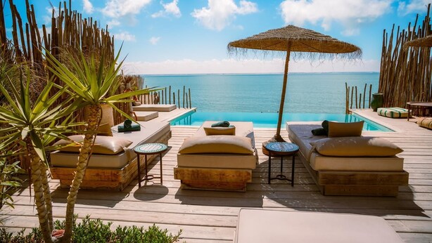 Terraza de madera con sillones de descanso y piscina con vista al mar.
