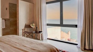 Habitación de hotel con un ventanal grande, una cama, una silla y una mesita con un objeto decorativo.