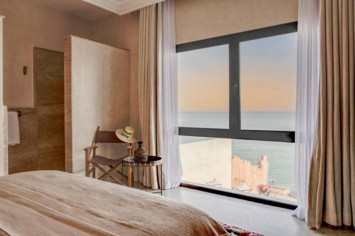 A hotel room with a large window, a bed, a chair, and a small table with a decorative item.