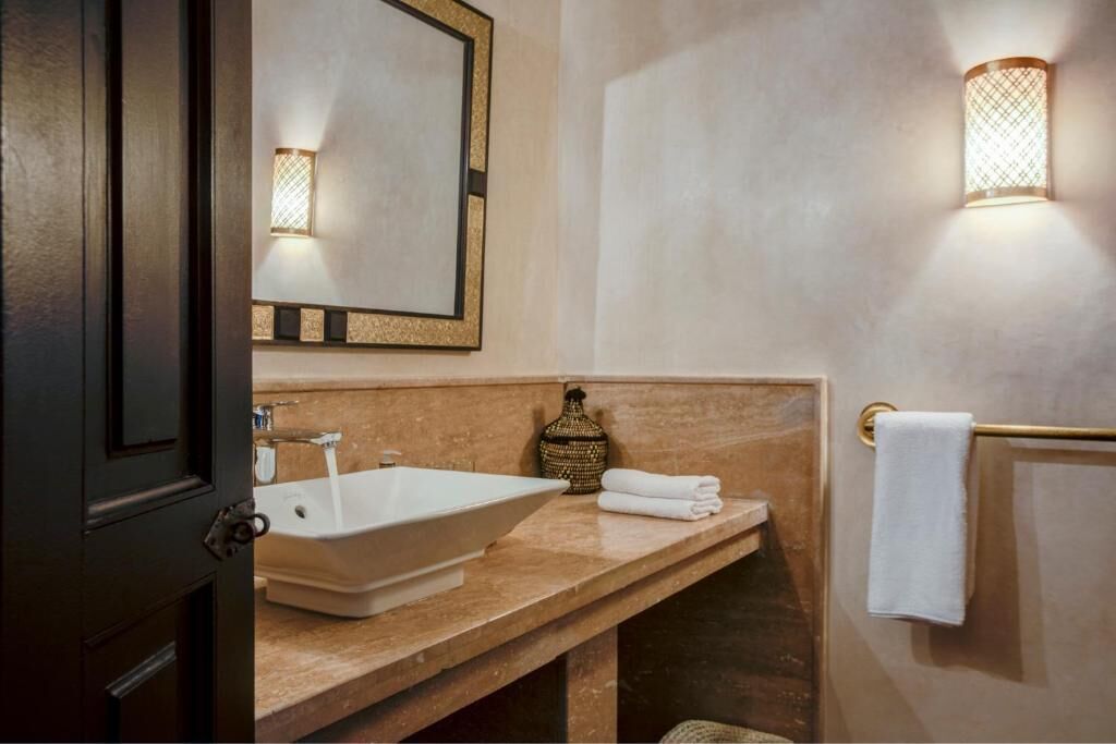 A bathroom with a large sink, a mirror, a towel rack, and a decorative vase.