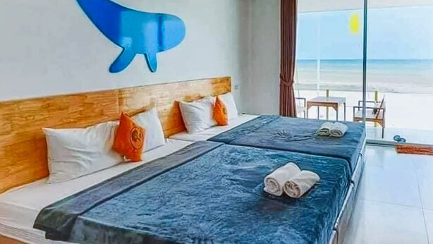 Habitación de hotel con dos camas, cabecera de madera y vista a la playa.