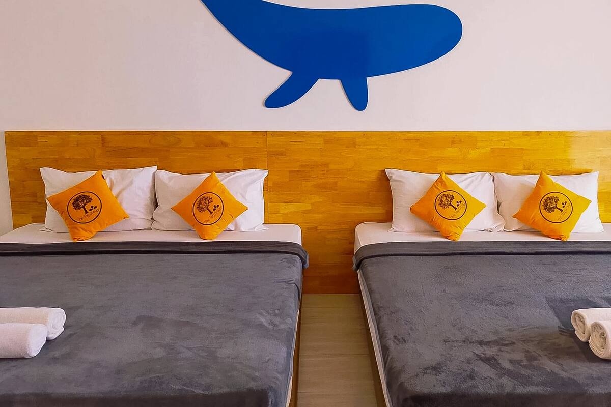 A hotel room with two beds, each with a grey bedspread and white pillows, some with a logo. A large blue animal silhouette is on the wall above the beds.