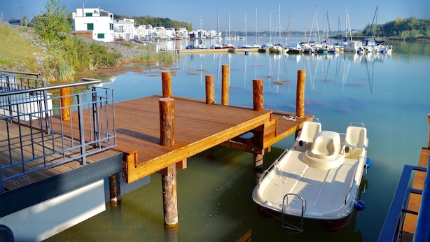 Un puerto deportivo con un muelle de madera, un barco pequeño y varios veleros al fondo.