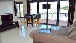 Una sala de estar moderna con una televisión de pantalla plana, un sofá, una mesa de centro de vidrio y una zona de comedor con sillas.