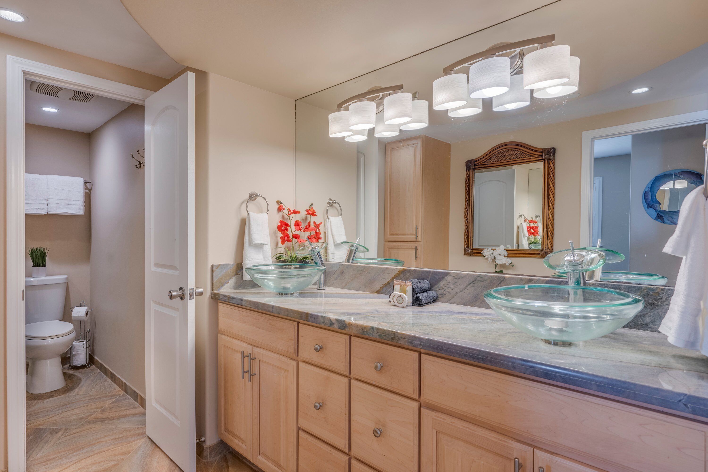 Un baño moderno con un lavabo de vidrio, muebles de madera y un espejo grande.