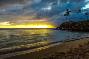 Uma praia com pôr do sol, mar calmo e palmeiras.