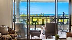 A balcony with a view of the ocean, wicker furniture, and a potted plant.