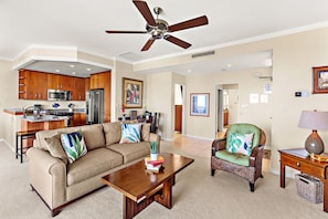 A spacious living room with a sofa, coffee table, and armchair, a kitchen with modern appliances, and a ceiling fan. - Kapalua Golf Villa, fresh updates and fairway view (Lahaina)