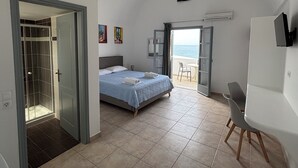 A bedroom with a bed, a shower, a balcony with a table and chairs, and a view of the sea. - Tarelis Beach Apartments & Studios (Santorini)