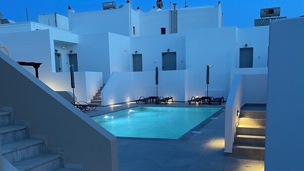 A rooftop pool area with white buildings, a pool, and steps leading to the pool. - Tarelis Beach Apartments & Studios (Santorini)