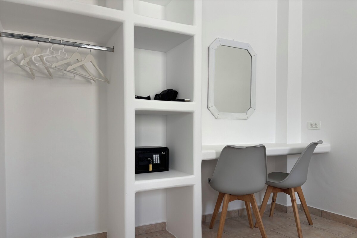 A white room with a wardrobe, a desk, two chairs, a mirror, and a safe.