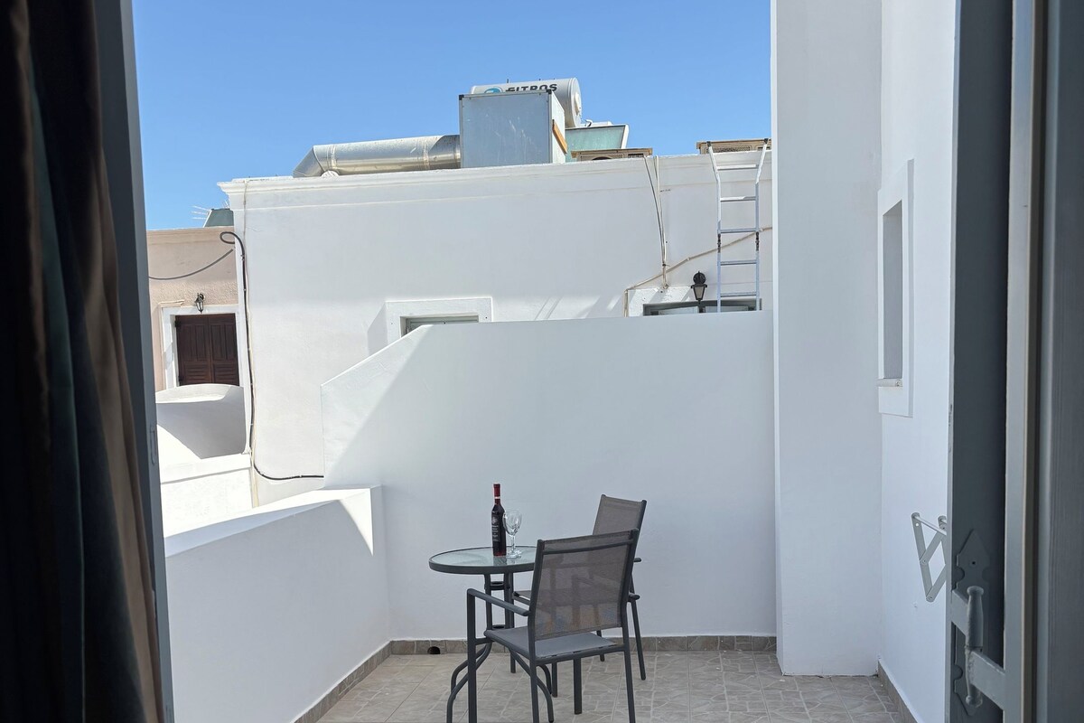 A balcony with a table and chairs, white walls, and a clear sky.