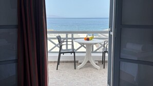 A room with a bed, a table with fruits, a chair, and a view of the sea. - Tarelis Beach Apartments & Studios (Santorini)
