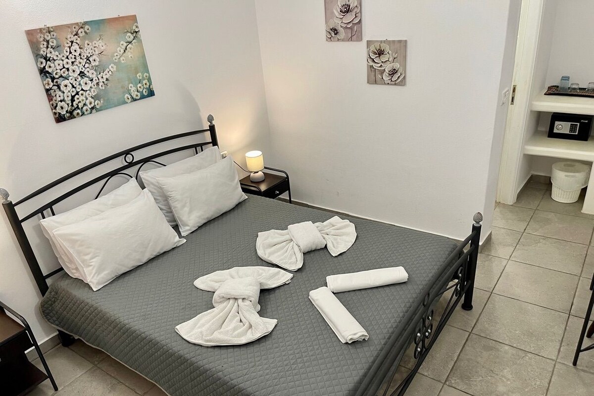A neatly made bed with pillows and towels, a bedside table with a lamp, and artwork on the walls.