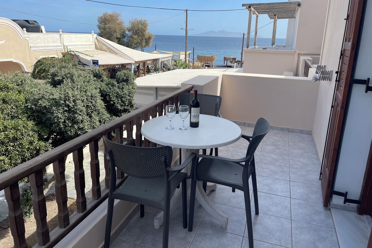 A balcony with a round table and chairs, overlooking a body of water and a mountainous landscape.