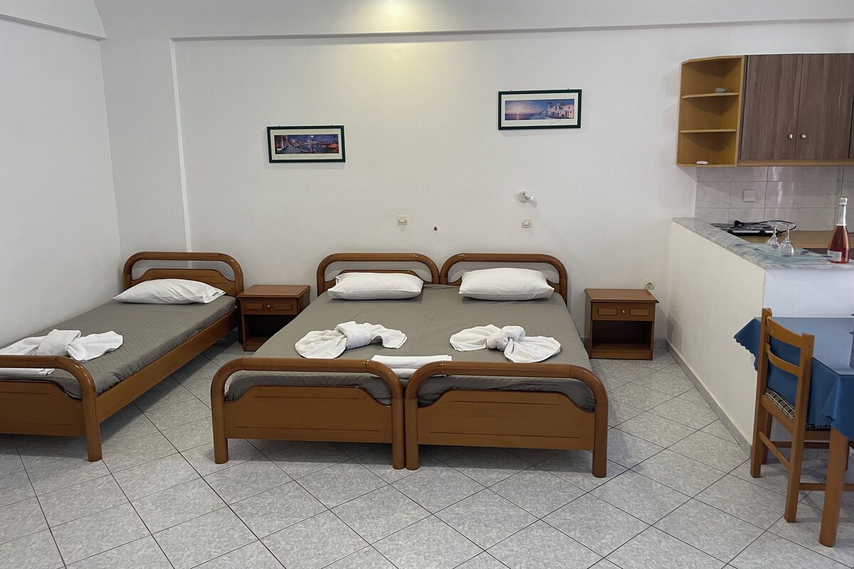 Una habitación con tres camas de madera, un pequeño rincón de cocina y dos cuadros en la pared.