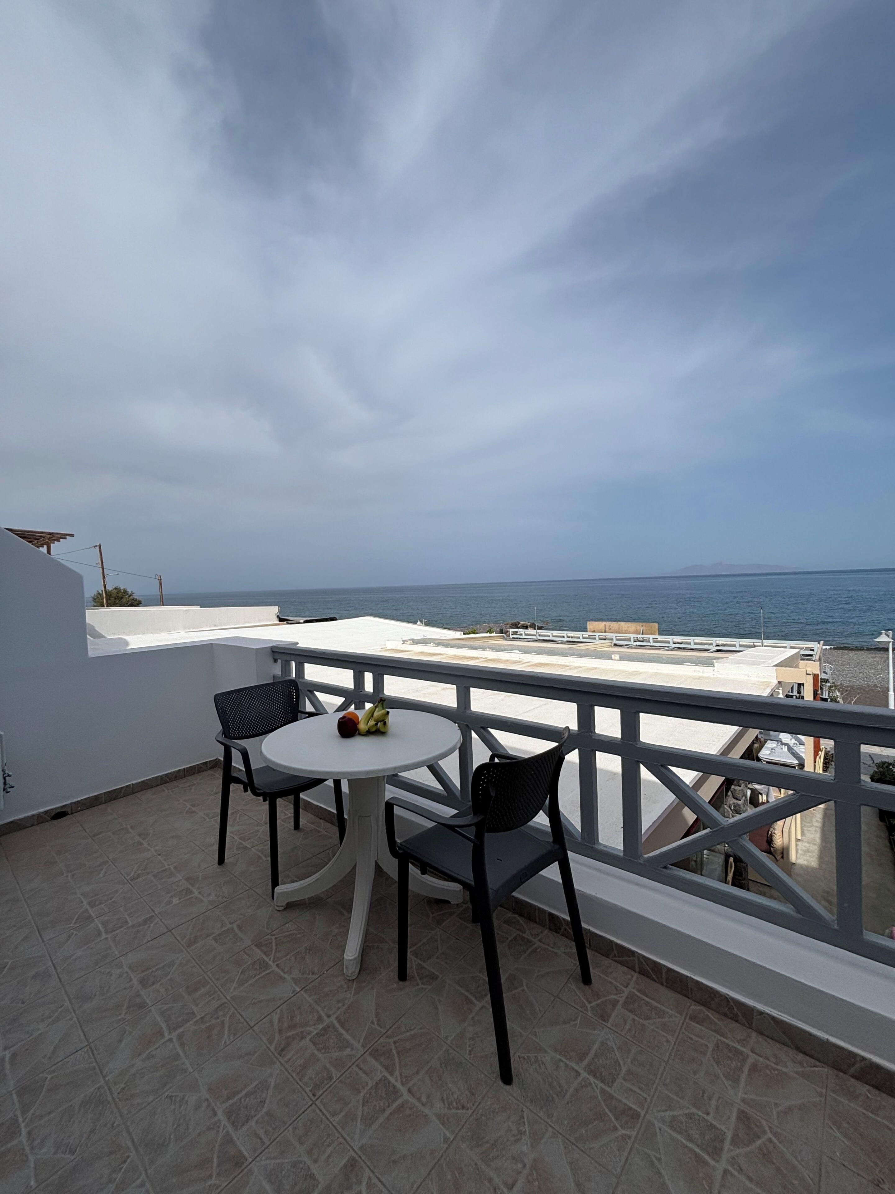 En balkon med et bord og stole, udsigt til havet og en fjerntliggende ø.
