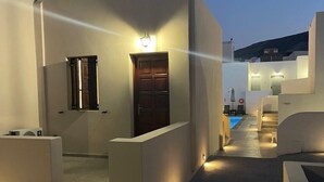 A modern building with a curved facade, a wooden door, and a small pool area. - Tarelis Beach Apartments & Studios (Santorini)