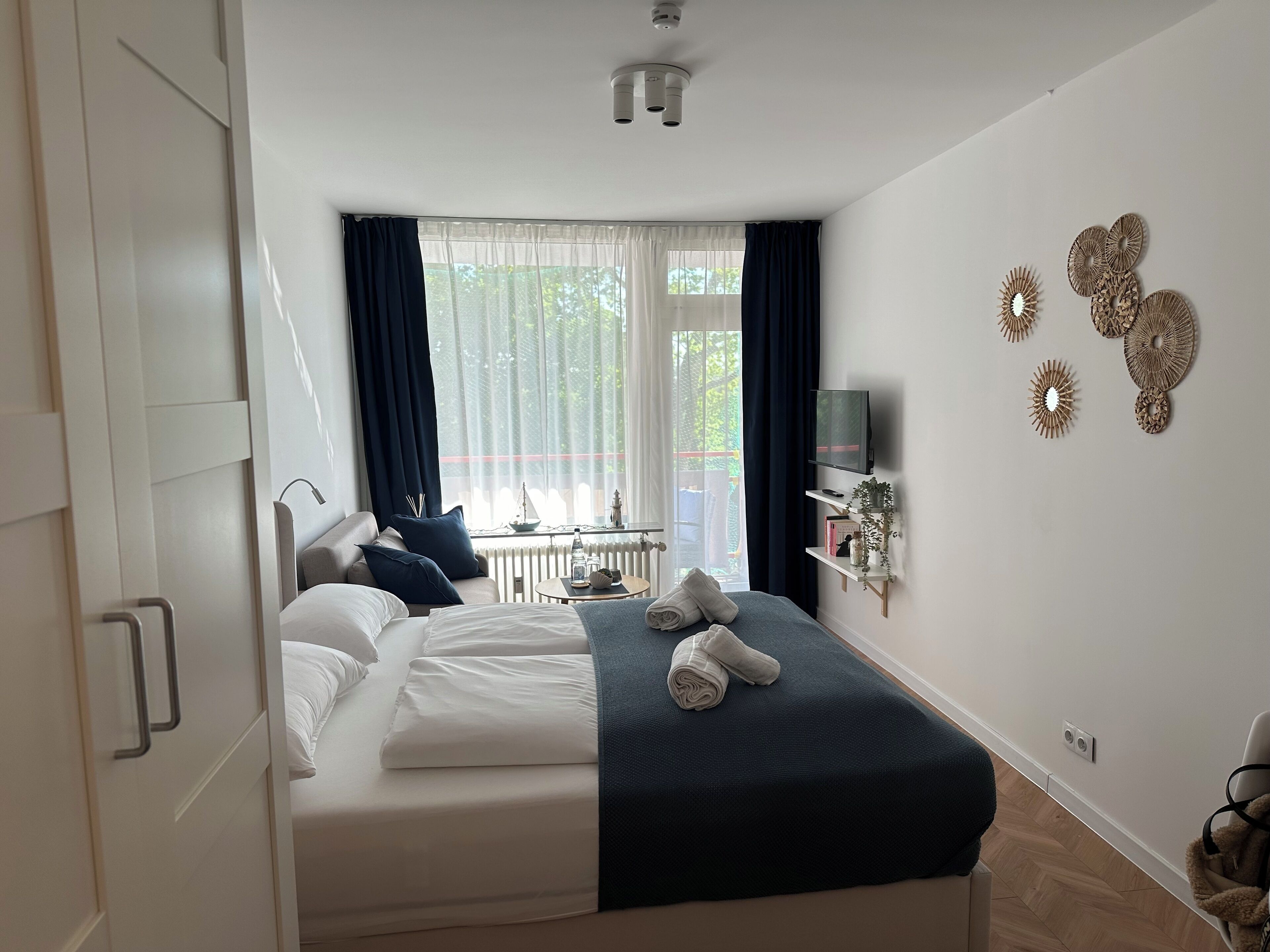 Un dormitorio ordenado con cama, mesita de noche y televisor instalado en la pared.