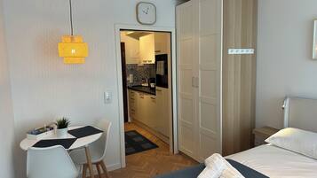 Een moderne hotelkamer met een bed, een bureau met stoel, een kledingkast, en een keukenruimte zichtbaar door een open deur.