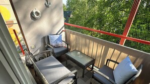 Un balcon agrémenté de meubles en osier, d’une table en verre et offrant une vue sur les arbres.