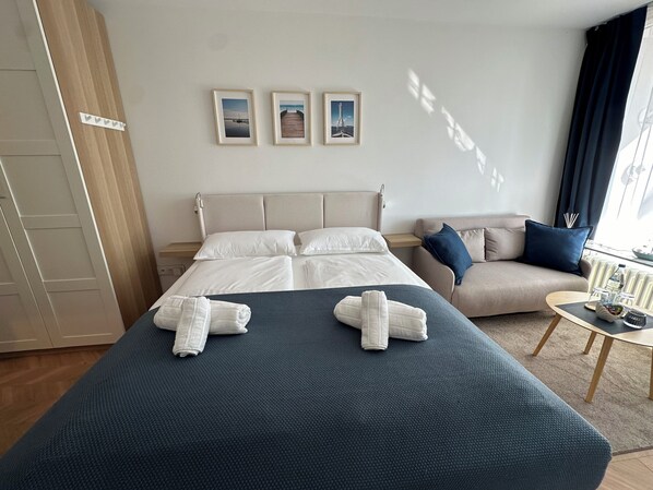 Habitación de hotel con cama, sofá y una mesita con una bandeja. En la pared hay tres cuadros enmarcados.