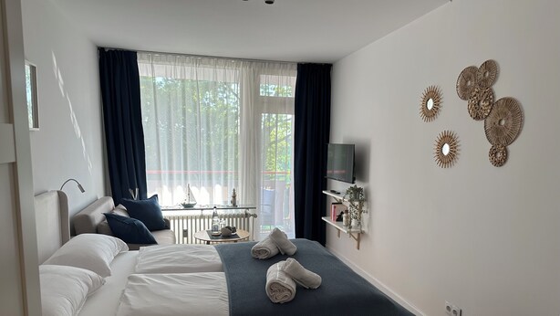 Une chambre d’hôtel avec un lit, une petite table avec une lampe, un téléviseur fixé au mur et des œuvres d’art décoratives accrochées au mur.