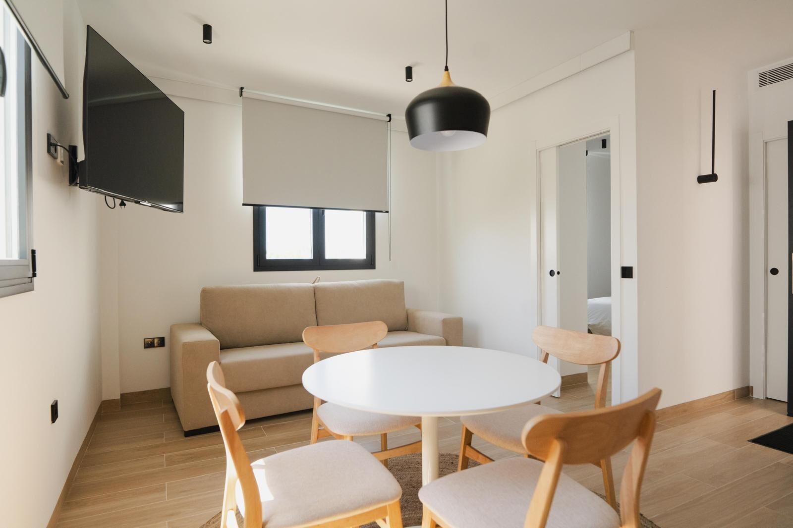Ein modernes Wohnzimmer mit einem beigefarbenen Sofa, einem runden weißen Tisch und Holzstühlen.