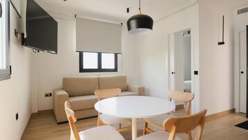 Ein modernes Wohnzimmer mit einem beigefarbenen Sofa, einem runden weißen Tisch und Holzstühlen.