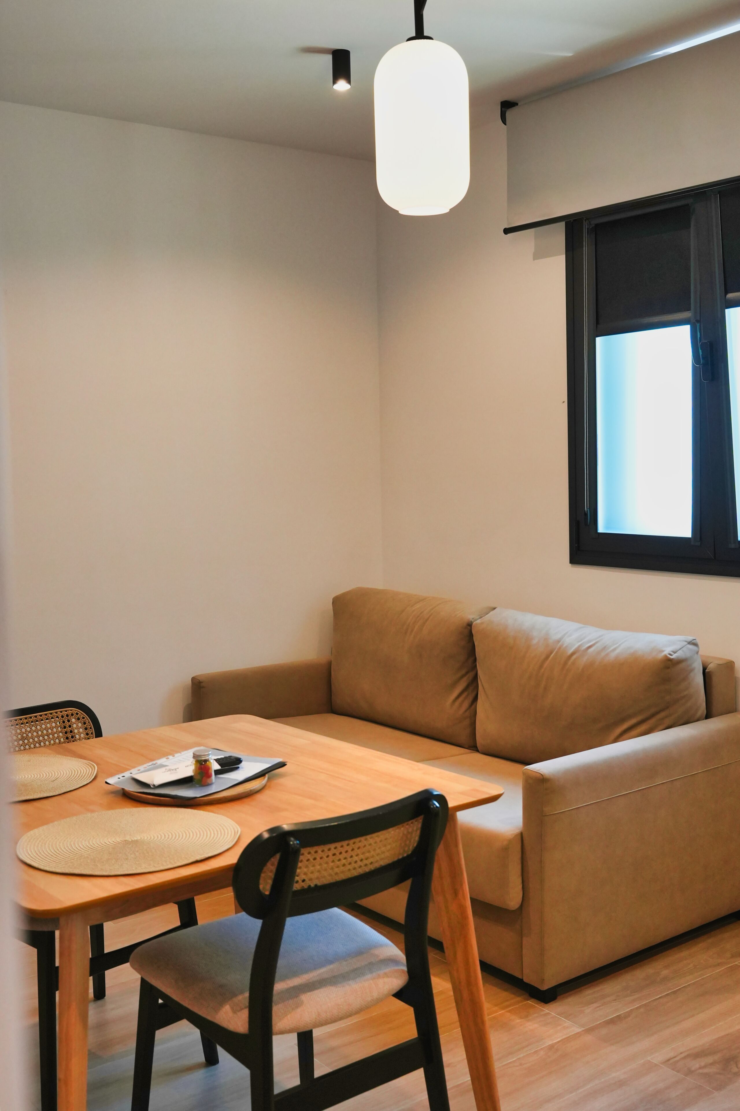 Et værelse med et træspisebord, en beige sofa, en enkelt stol og en loftslampe.