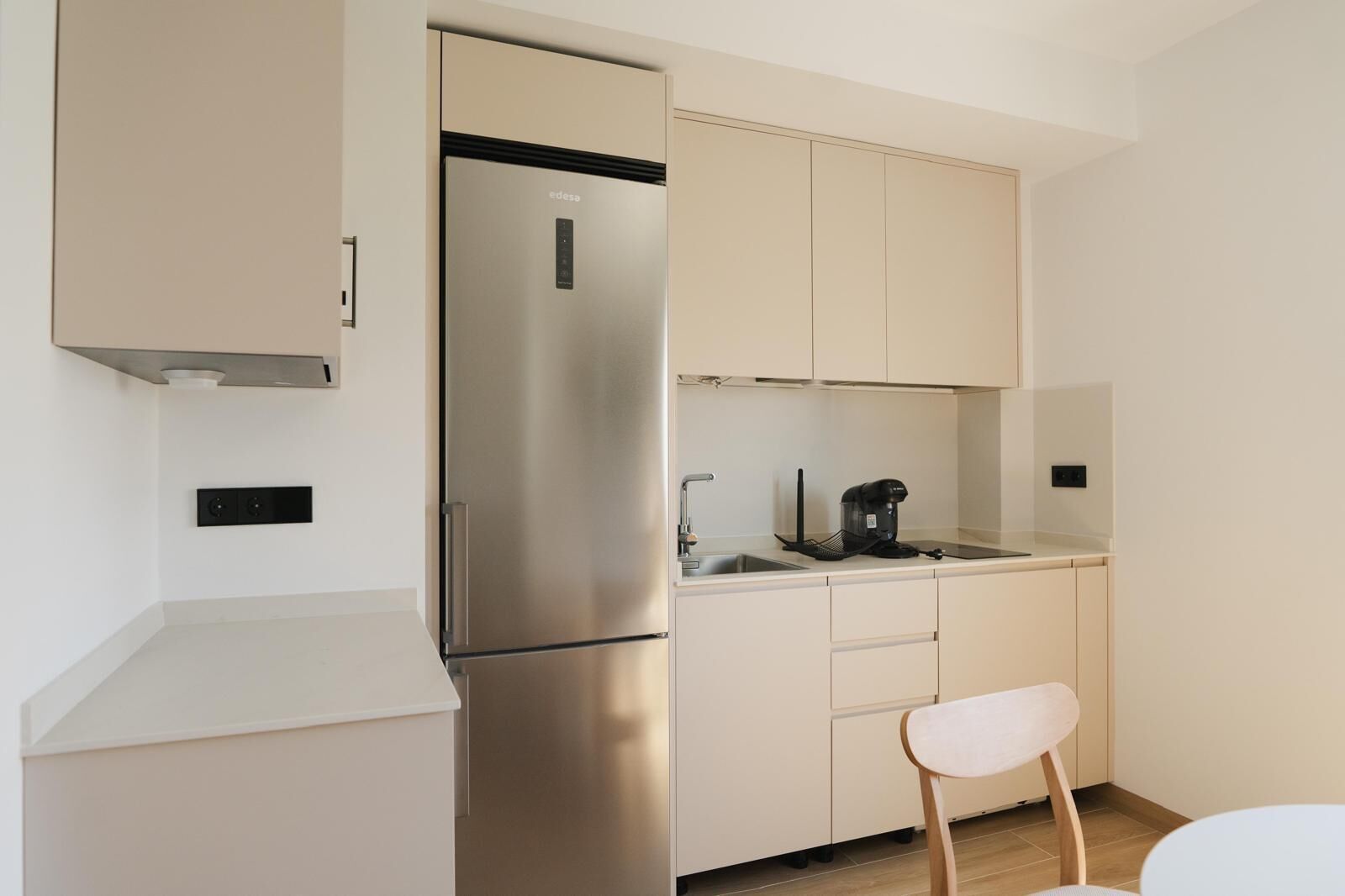 Una cocina compacta con un refrigerador de acero inoxidable, una cafetera y una sola silla.