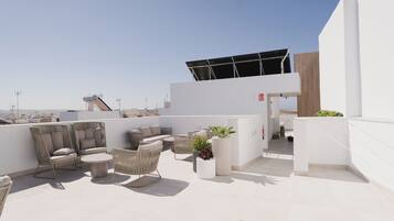Una terraza en la azotea con mobiliario exterior, un panel solar y vistas del horizonte de la ciudad.