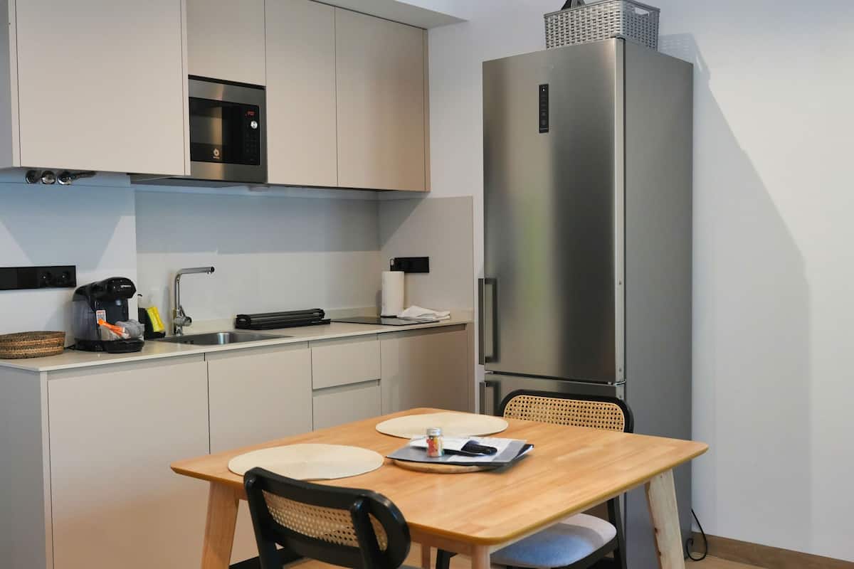Cocina compacta con microondas integrado, refrigerador de acero inoxidable, cafetera y comedor con mesa y sillas.