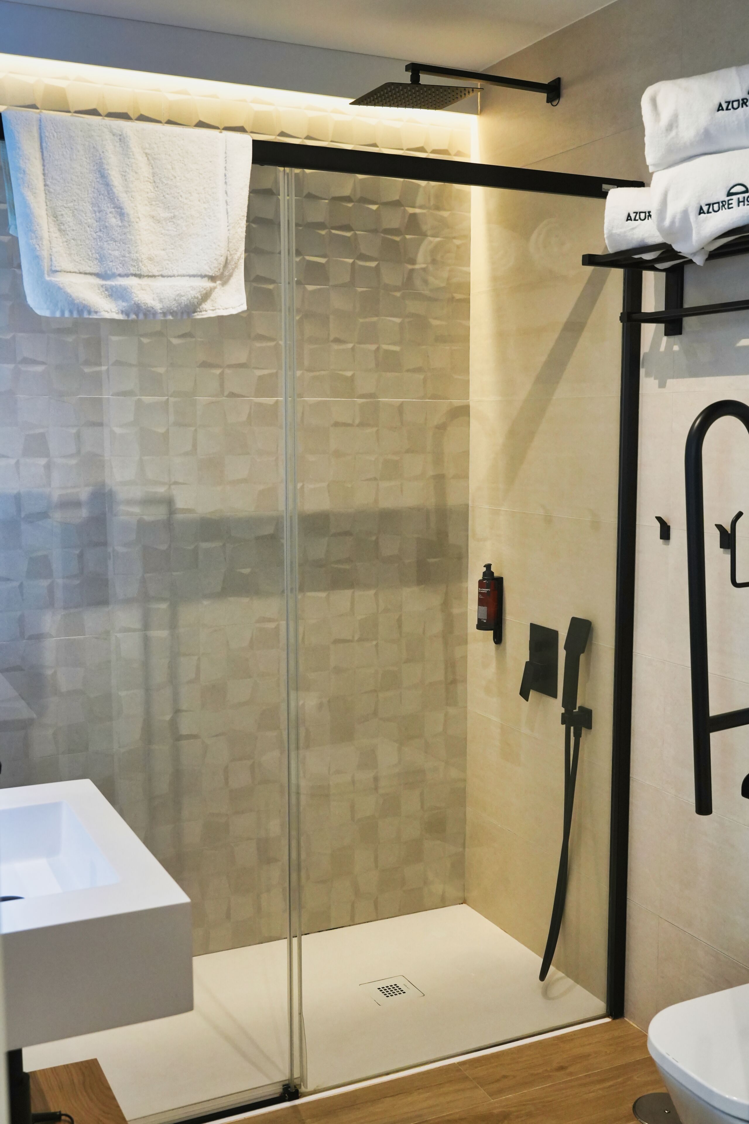 A modern bathroom with a glass-enclosed shower, a white sink, and a towel rack with branded towels.