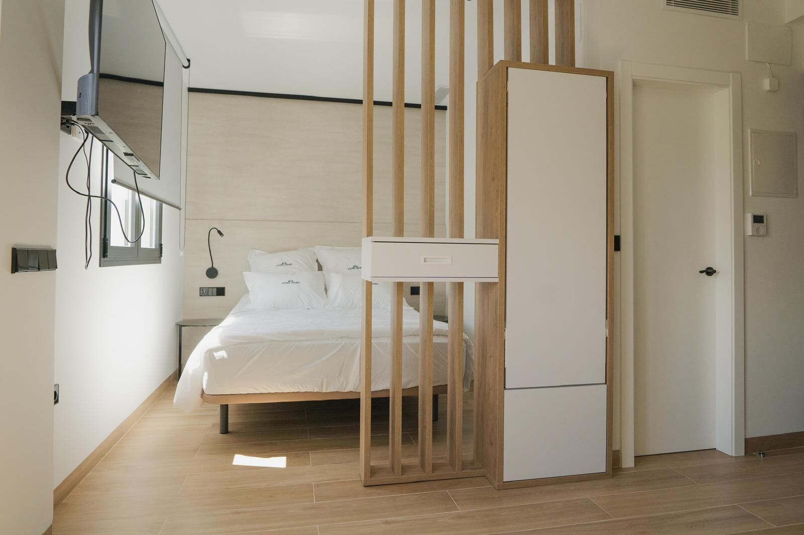 Ein modernes Schlafzimmer mit einem Bett, einer Holztrennwand und einem weißen Kleiderschrank.