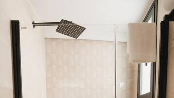 Ducha a pie con mampara de vidrio, azulejos color beige, un cabezal de ducha manual y una ventana pequeña.