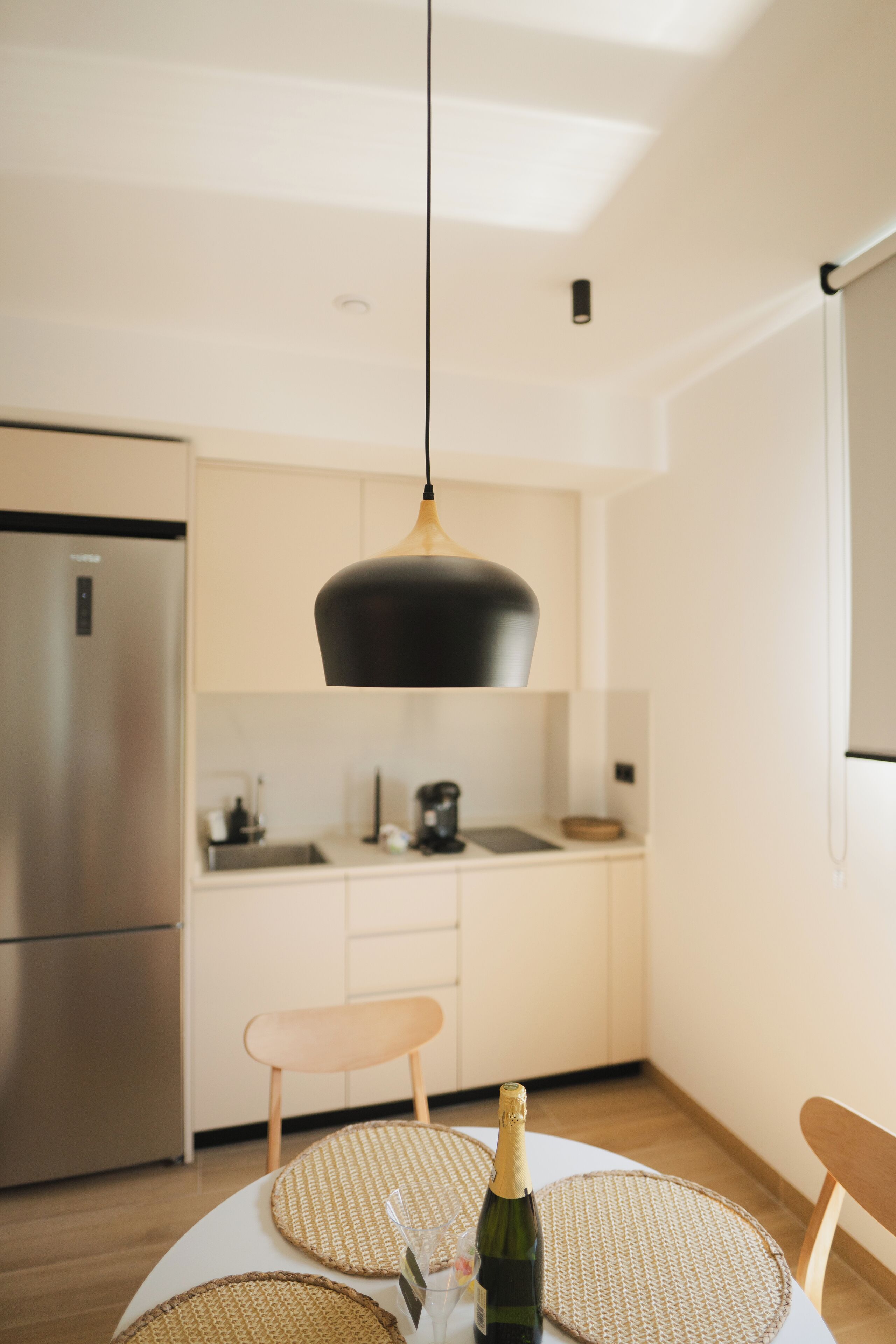 Una cocina moderna con un refrigerador de acero inoxidable, una mesa de comedor de madera y una lámpara colgante arriba.