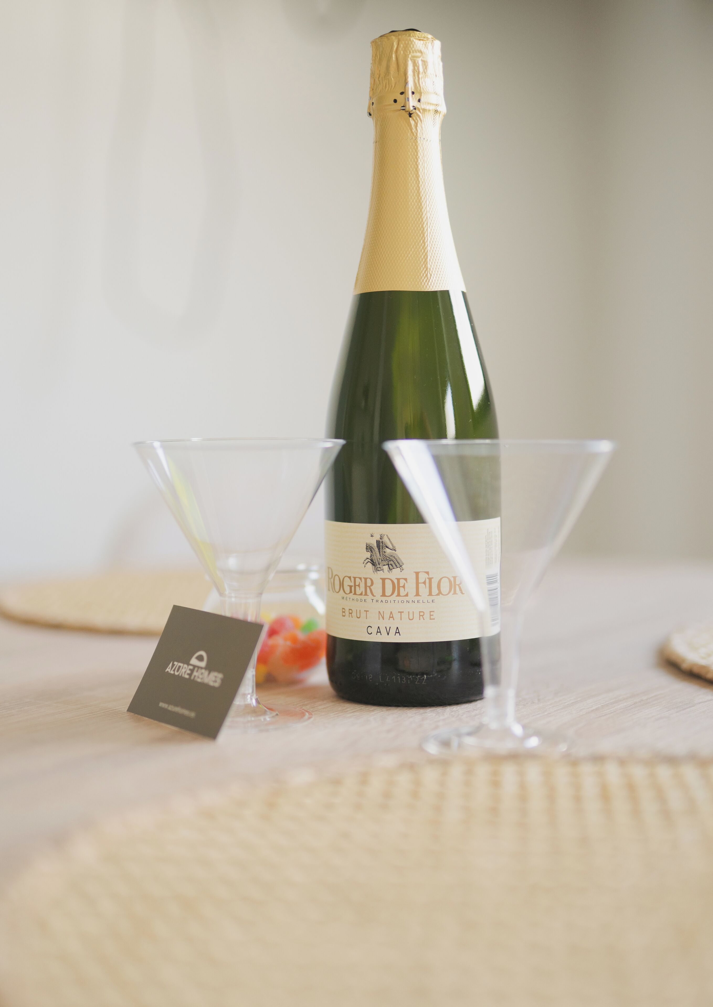 Uma garrafa de vinho com etiqueta, dois copos de martini vazios e um pequeno cartão sobre uma superfície de madeira.