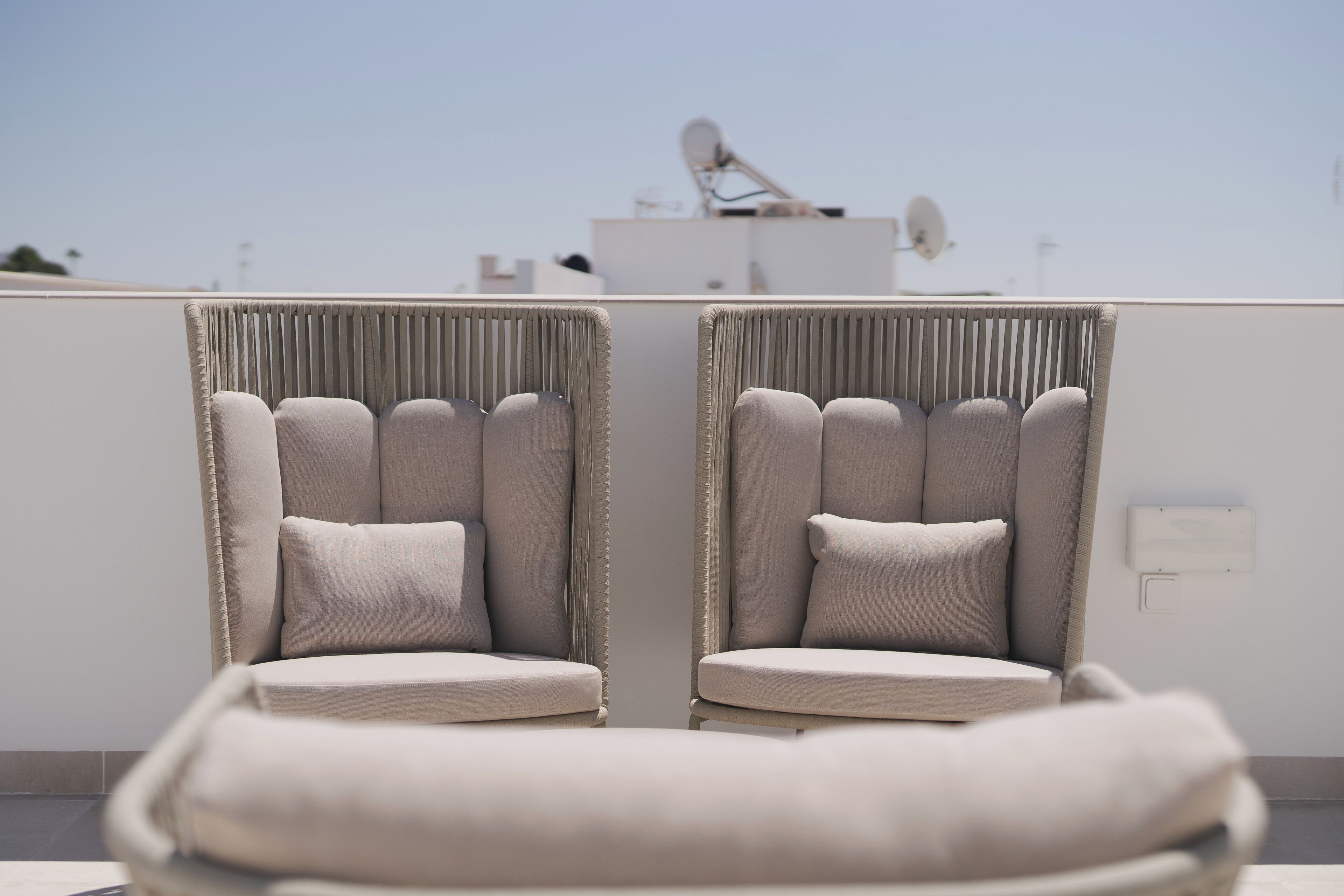 Twee beige fauteuils met kussens op een terras op een dak.