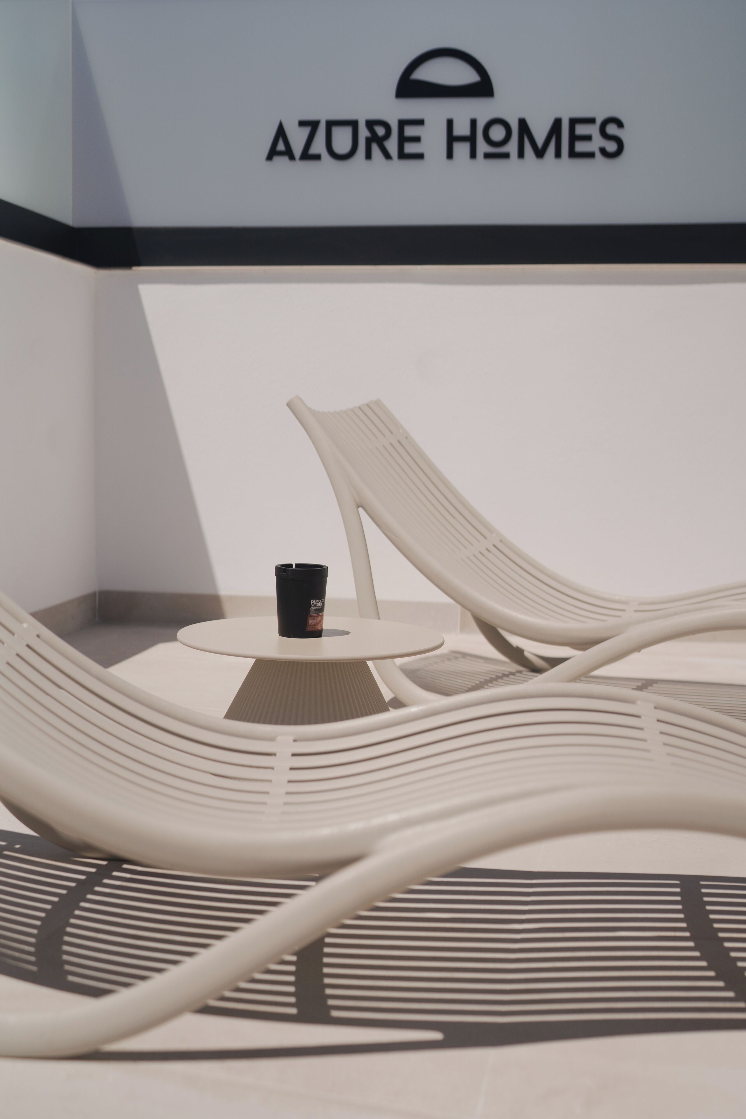 Ein Loungebereich mit einem Tisch und zwei Lounge-Sesseln, eine Kaffeetasse auf dem Tisch und ein Schild mit der Aufschrift 'AZURE HOMES'.