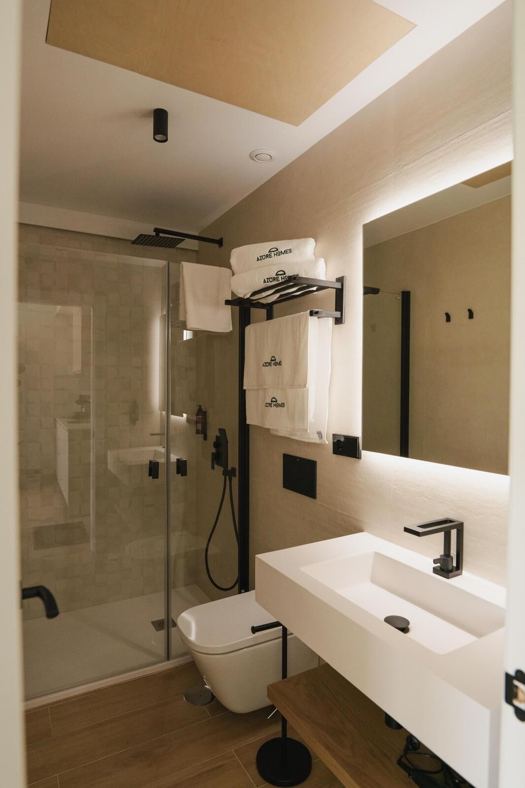 Un baño moderno con cabina de ducha de vidrio, un lavabo blanco con grifo negro y un espejo grande sobre el lavabo.